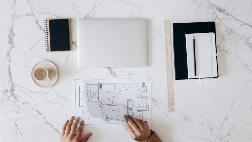 marmeren tafel met laptop, notitieboek, koffie en persoon die plan tekent