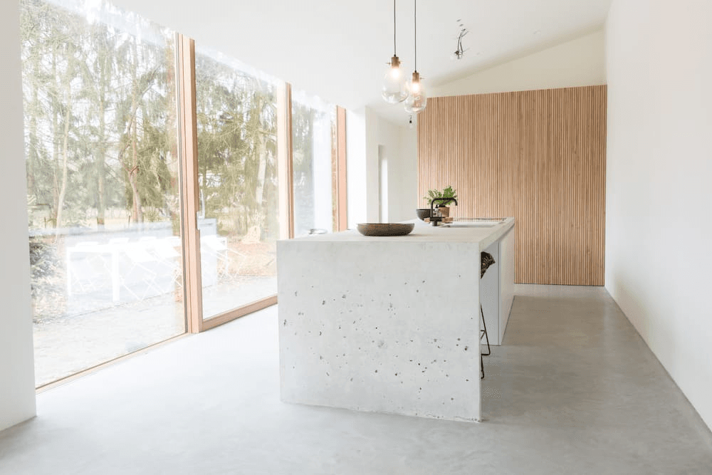 strakke lichte keuken met licht hout, betonnen gietvloer en keukeneiland uit natuursteen en grote schuifraam